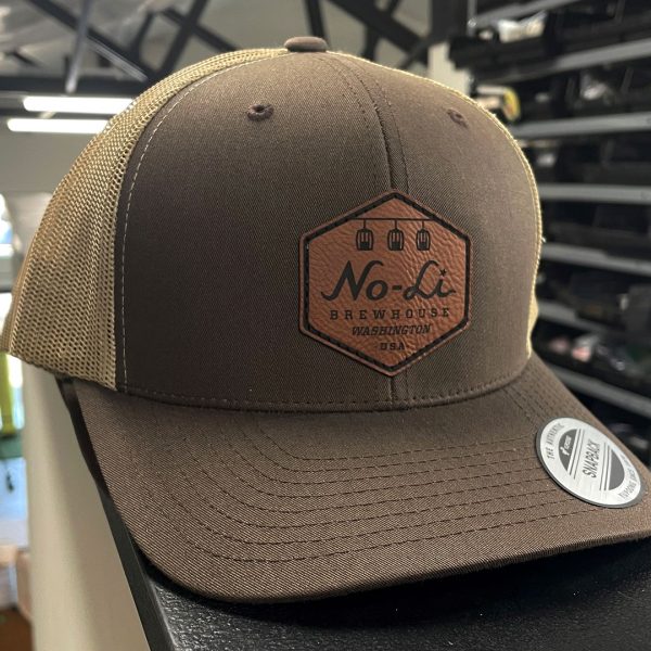 Brown trucker hat with a No-Li Brewhouse hexagon leather patch